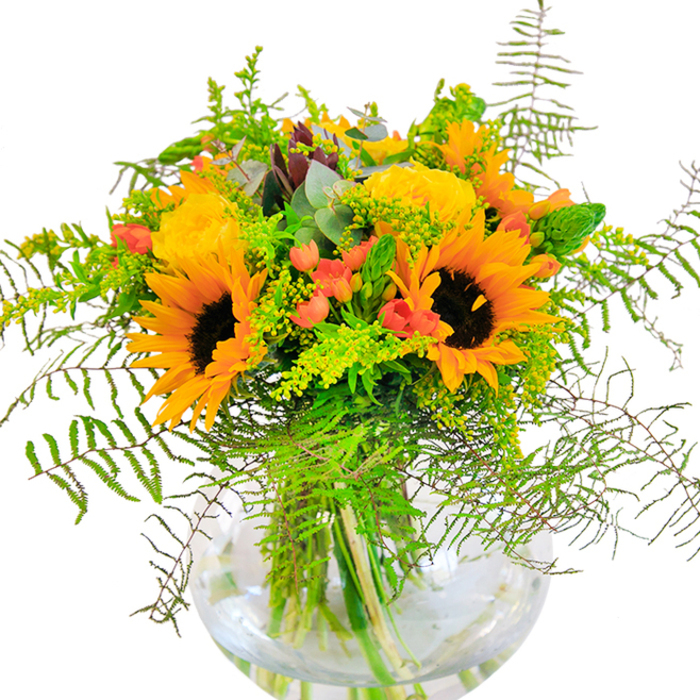 From the very first glance, this Malden Rushett bouquet feels like a cheerful beacon of warmth and abundance. Dominated by bold sunflowers and golden garden roses, the arrangement radiates sunlight, their petals reaching outward with exuberance and promise - as if welcoming guests to a garden party near Prince's Coverts. Twining greenery and delicate fern fronds create a sense of dynamic movement, with their airy forms spilling gracefully around the vibrant blooms, much like wild grasses beside woodland paths. Dotted among the foliage, crimson hypericum berries gleam like hidden treasures, injecting playful bursts of colour and contrast. Soft sprigs of goldenrod and slender green stems weave through the display, amplifying its natural, carefree feel. Eucalyptus leaves, cool and slightly blue, nestle discreetly amidst the richer greens, releasing a fresh, restorative scent. The round, transparent vase supports the arrangement like a clear pool, showing off every lively stem and amplifying the sense of life and clarity. This detailed composition is perfect for celebratory occasions - birthdays, congratulations, or simply bringing a splash of joy to a Malden Rushett home - and showcases a deep appreciation for both the changing seasons and the natural beauty found throughout the local area.