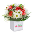Fresh and full of optimism, this bouquet is a graceful blend of flowers arranged by a trusted Malden Rushett florist, echoing the peaceful countryside charm found nearby. The gathering features coral, peach, and striking red carnations-each petal richly textured and softly ruffled, evoking a sense of comfort and joy. Intermixed are crisp white daisies with sunny green-yellow centres; their bright faces bring a touch of spring-like laughter to the design, feeling right at home amid the open spaces of Malden Rushett. Delicate tufts of baby's breath float between the bolder blossoms, adding airiness and a quiet, innocent beauty. Along one side, a few unopened buds dusted in soft purple appear, whispering of growth and hopefulness. Wrapping the arrangement, an abundance of deep, glossy green foliage forms a luxurious collar, cradling the flowers and lending structure, much like the resilient hedges that line the village lanes. The bouquet stands proud within its pristine, square white carrier bag, complete with silk ribbon handles for easy delivery to homes or celebrations from Leatherhead Road to Rushett Crescent. Set on a pure white background, the artistry and heartfelt care of the local florist shines through, making this arrangement ideal for birthdays, congratulations, or simply brightening a friend's day in Malden Rushett.